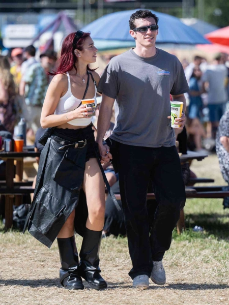 Dua Lipa walked around the fairgrounds at Glastonbury Music Festival holding hands with her boyfriend Callum Turner while wearing a high-slit skirt and slouchy boots. See their coordinating couple's looks here.