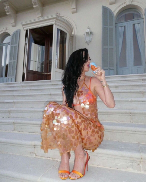 Katy Perry shared videos and photos of her posing in a tiny orange string bikini on a balcony in posts shared to Instagram and TikTok. The "California Gurls" singer, who had "Teenage Dream" playing in the background, later added a sheer sequined cover-up as she promoted her De Soi non-alcoholic beverage brand.
