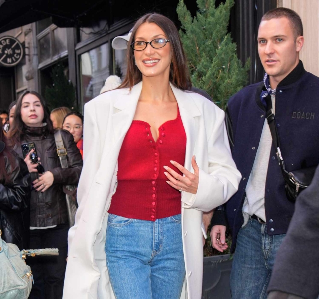 Bella Hadid leaned into the holiday office siren trend as she styled festive knits with winter white outerwear and black glasses on Saturday, December 14. See her outfit, here.